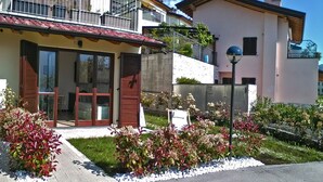 Un edificio residenziale con un balcone, una porta con persiane e un piccolo giardino con piante.