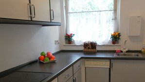 Een keuken met witte kastjes, een zwart aanrecht, een vaatwasser en een raam met gordijnen.