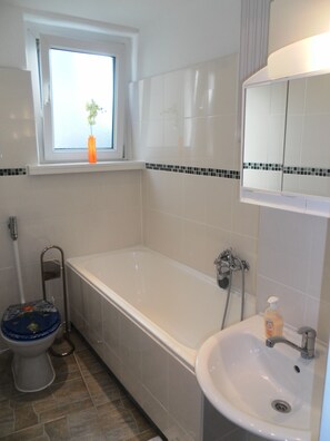 A bathroom with a bathtub, toilet, sink, and a window with a plant. - Apartment in Berlin near Potsdamer Platz (Berlin)