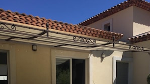 Un patio exterior con una pérgola, un área de descanso al aire libre color negro y un techo de baldosas.