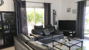 Una sala de estar moderna con un sofá de cuero, una mesa de centro de vidrio, un televisor y un aparador con cristalería.