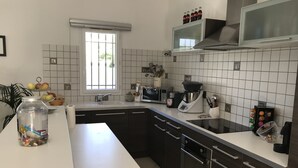 Una cocina moderna con encimera blanca, electrodomésticos de acero inoxidable y una ventana con rejas.