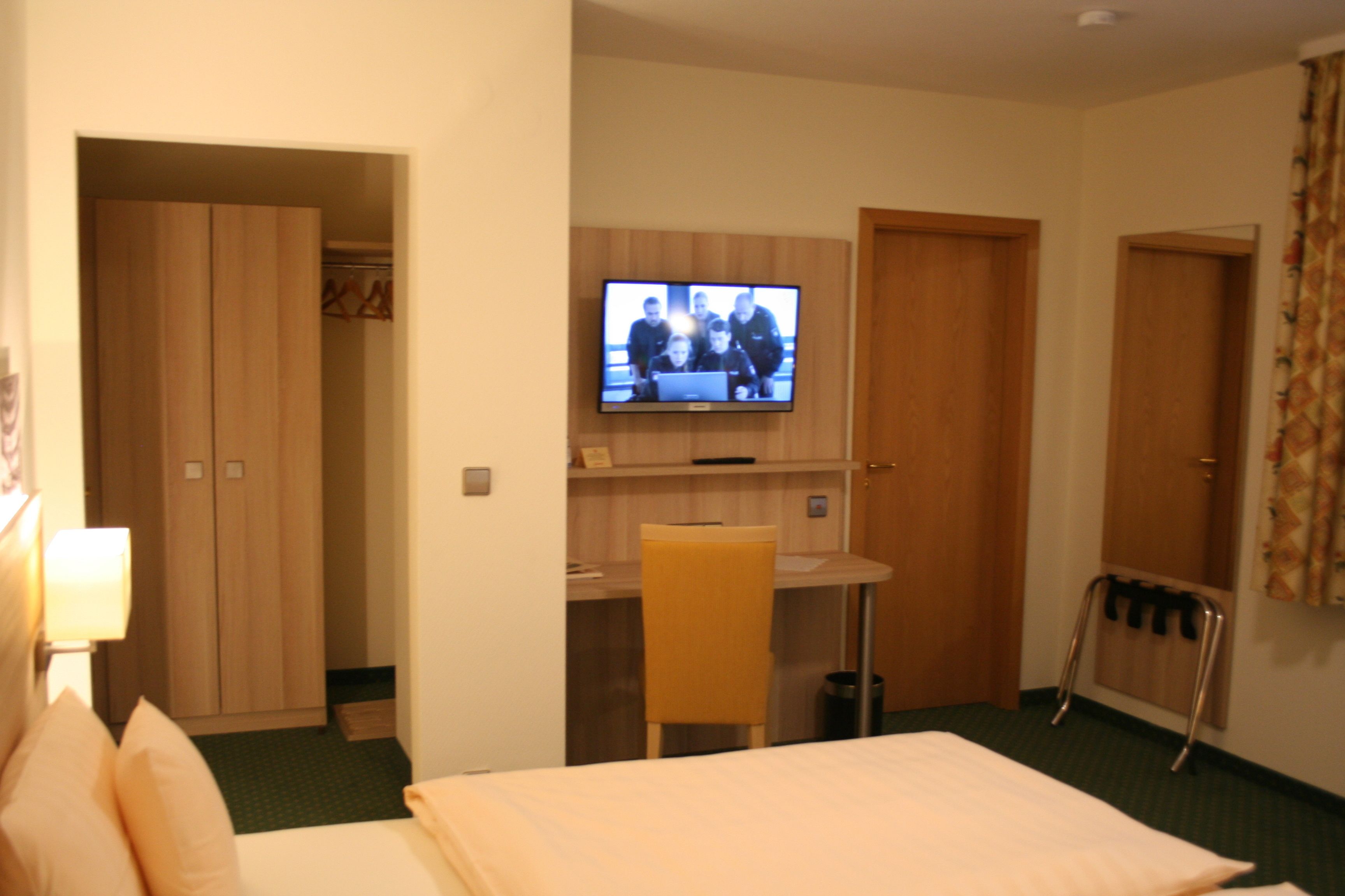 Een hotelkamer met een bed, een bureau met stoel, een aan de muur bevestigde televisie en een kledingkast.