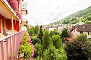A balcony with pink flowers, a view of a town with houses and trees, and a hill in the background. - Hotel Sonnenhof (Bad Wildbad)