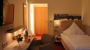 A hotel room with a bed, a desk with a lamp, a TV, and a painting on the wall. - Hotel Sonnenhof (Bad Wildbad)