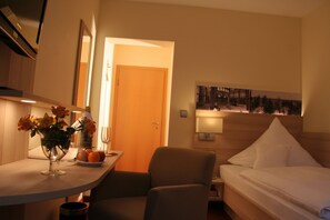 A hotel room with a bed, a bedside table with a vase of flowers, a chair, and a painting on the wall. - Hotel Sonnenhof (Bad Wildbad)
