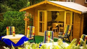 A wooden cabin with a porch, two chairs, a table, and a small dining area. - Hotel Sonnenhof (Bad Wildbad)