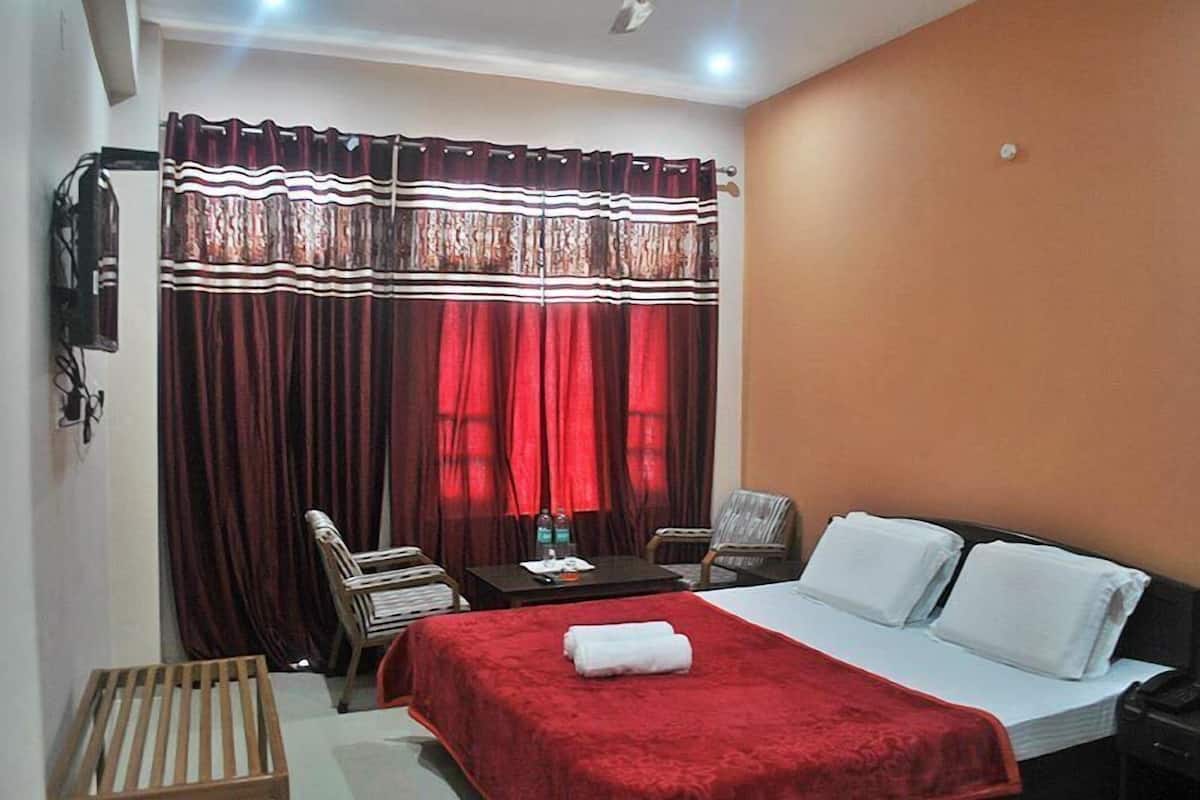 A hotel room with a bed, a desk, two chairs, a small table, and a window with curtains.