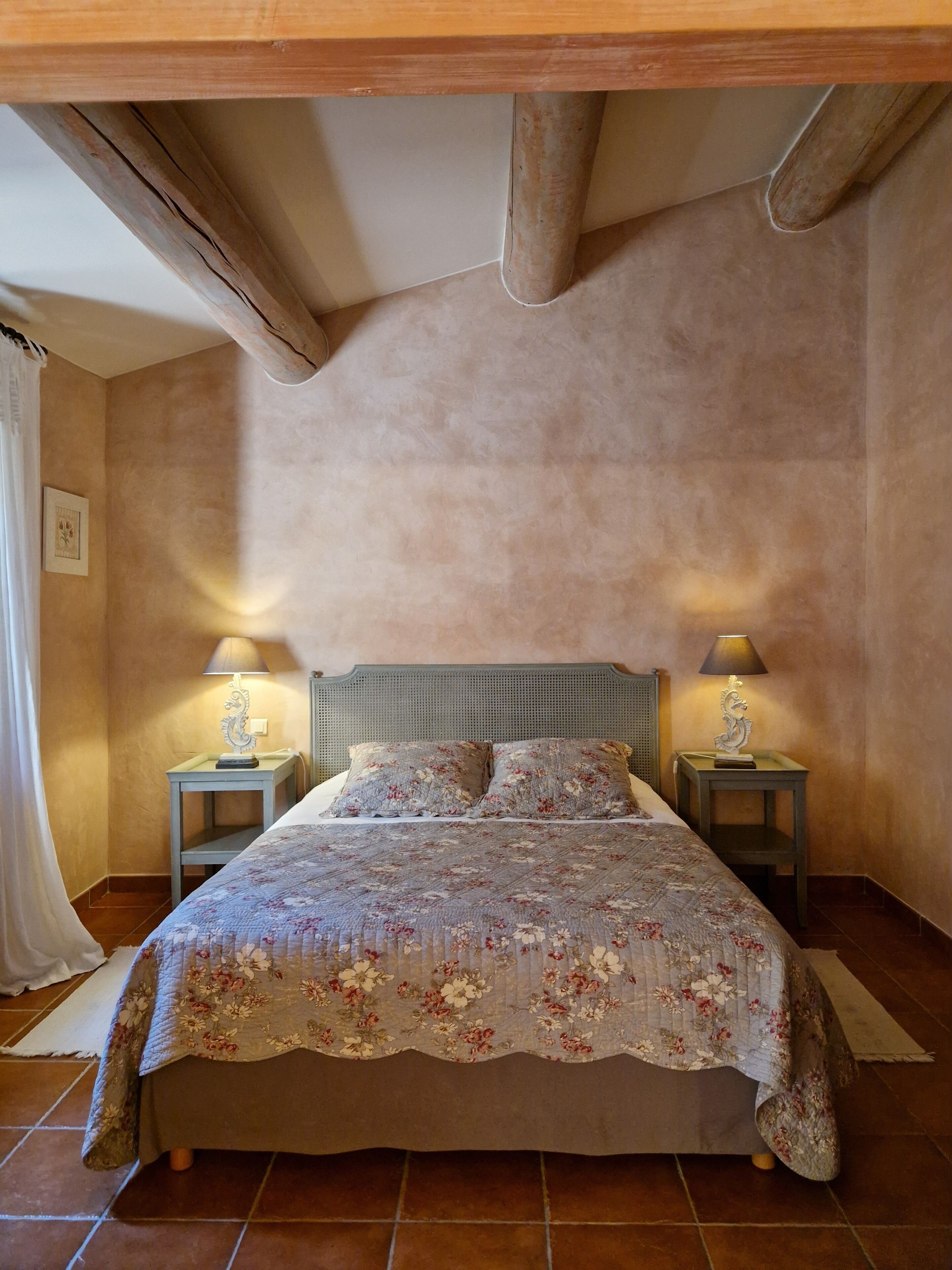 Une chambre à coucher avec un lit, deux tables de chevet, une tête de lit et un rideau.