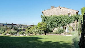 A stone building with ivy-covered walls, a well-maintained lawn, and a pergola structure in the background. - Hotel Mas de Fauchon (Saint-Cannat)