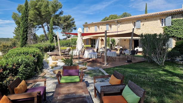 An outdoor seating area with tables and chairs, surrounded by greenery and a stone building. - Hotel Mas de Fauchon (Saint-Cannat)