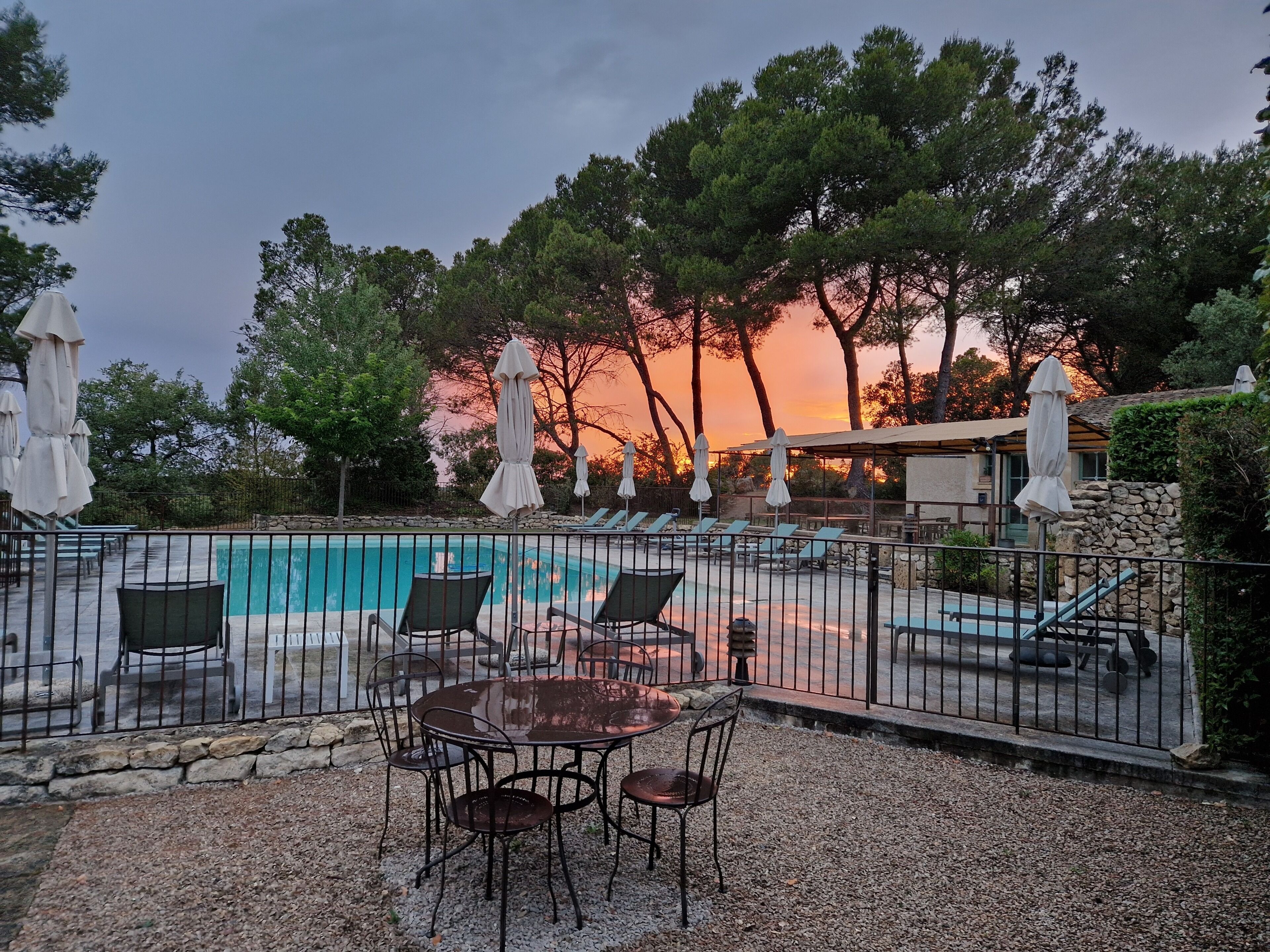 A poolside area with a table and chairs, surrounded by umbrellas and a stone wall.