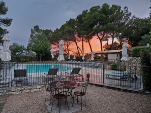A poolside area with a table and chairs, surrounded by umbrellas and a stone wall. - Hotel Mas de Fauchon (Saint-Cannat)