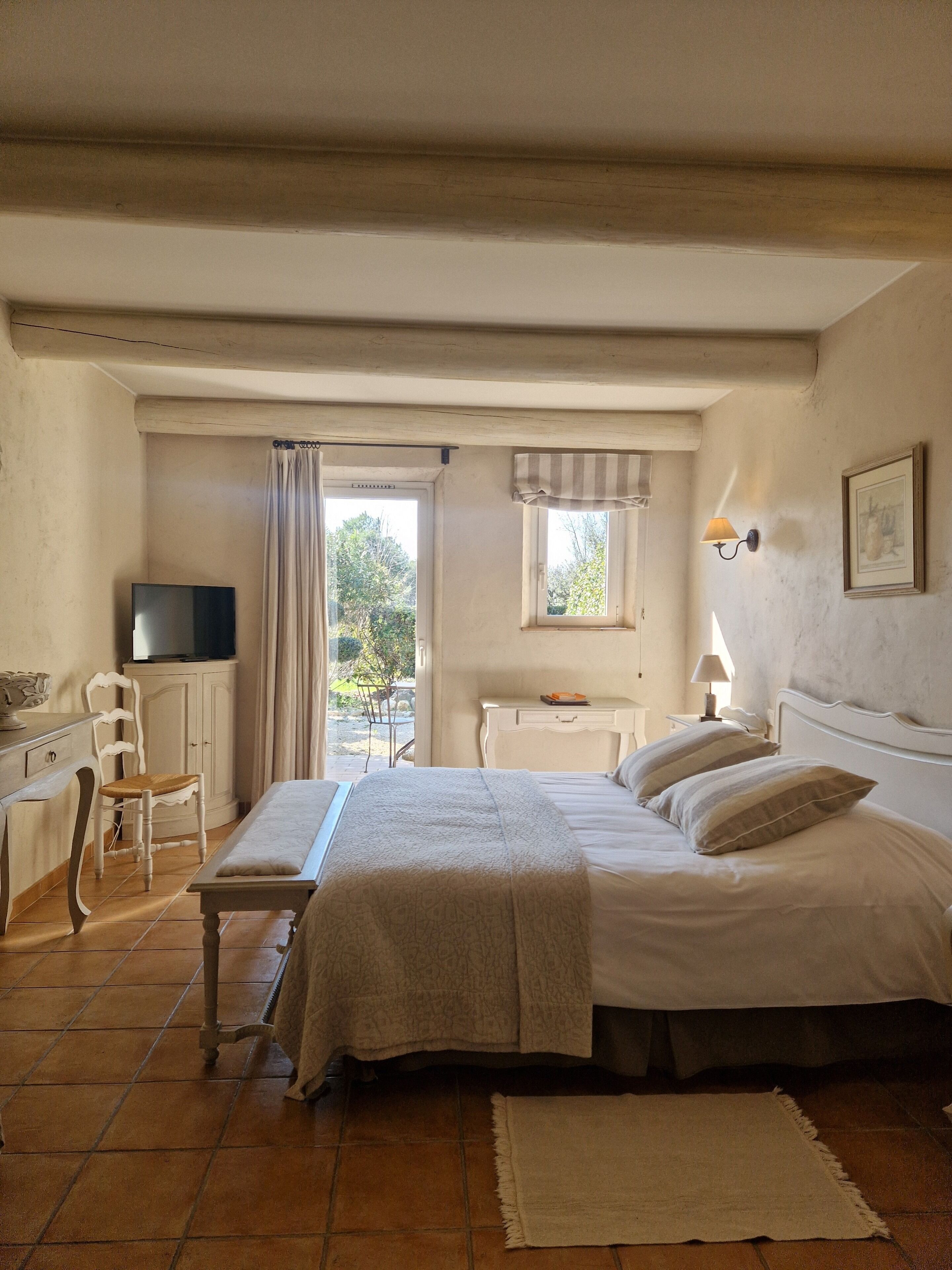 A bedroom with a bed, a desk, a chair, a television, and a window with curtains.