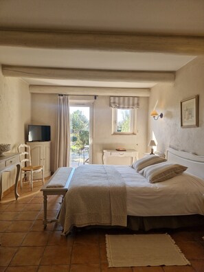 A bedroom with a bed, a desk, a chair, a television, and a window with curtains. - Hotel Mas de Fauchon (Saint-Cannat)