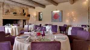 A restaurant with round tables, purple chairs, and a fireplace. - Hotel Mas de Fauchon (Saint-Cannat)