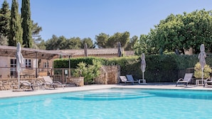 A clear swimming pool with lounge chairs and umbrellas, surrounded by stone walls and greenery. - Hotel Mas de Fauchon (Saint-Cannat)