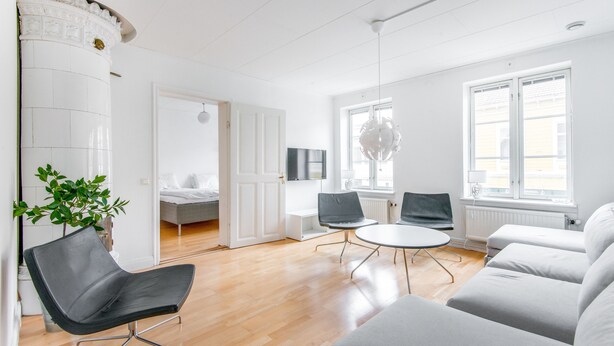 Un salón moderno con suelo de madera, un sillón de cuero negro, un sofá gris, una mesa blanca y una planta en maceta.