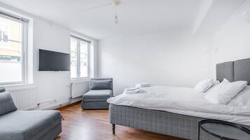 A modern bedroom with a bed, a grey armchair, a small table, and a TV mounted on the wall.
