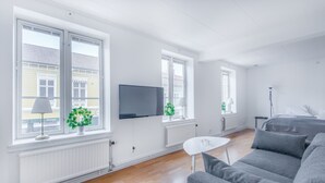 Una sala de estar moderna con un sofá gris, un televisor de pantalla plana montado en la pared y una pequeña mesa blanca.