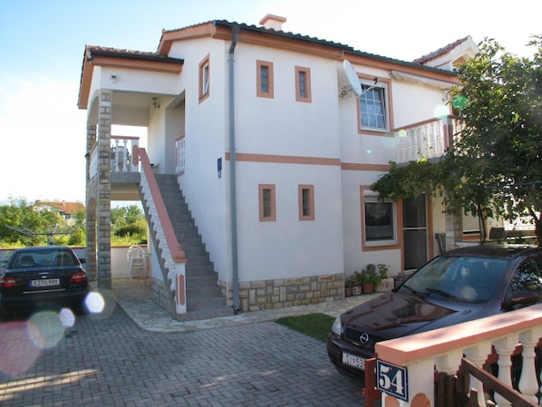 A two-story house with a staircase, a satellite dish, and two parked cars. - Apartments Galic (Nin)