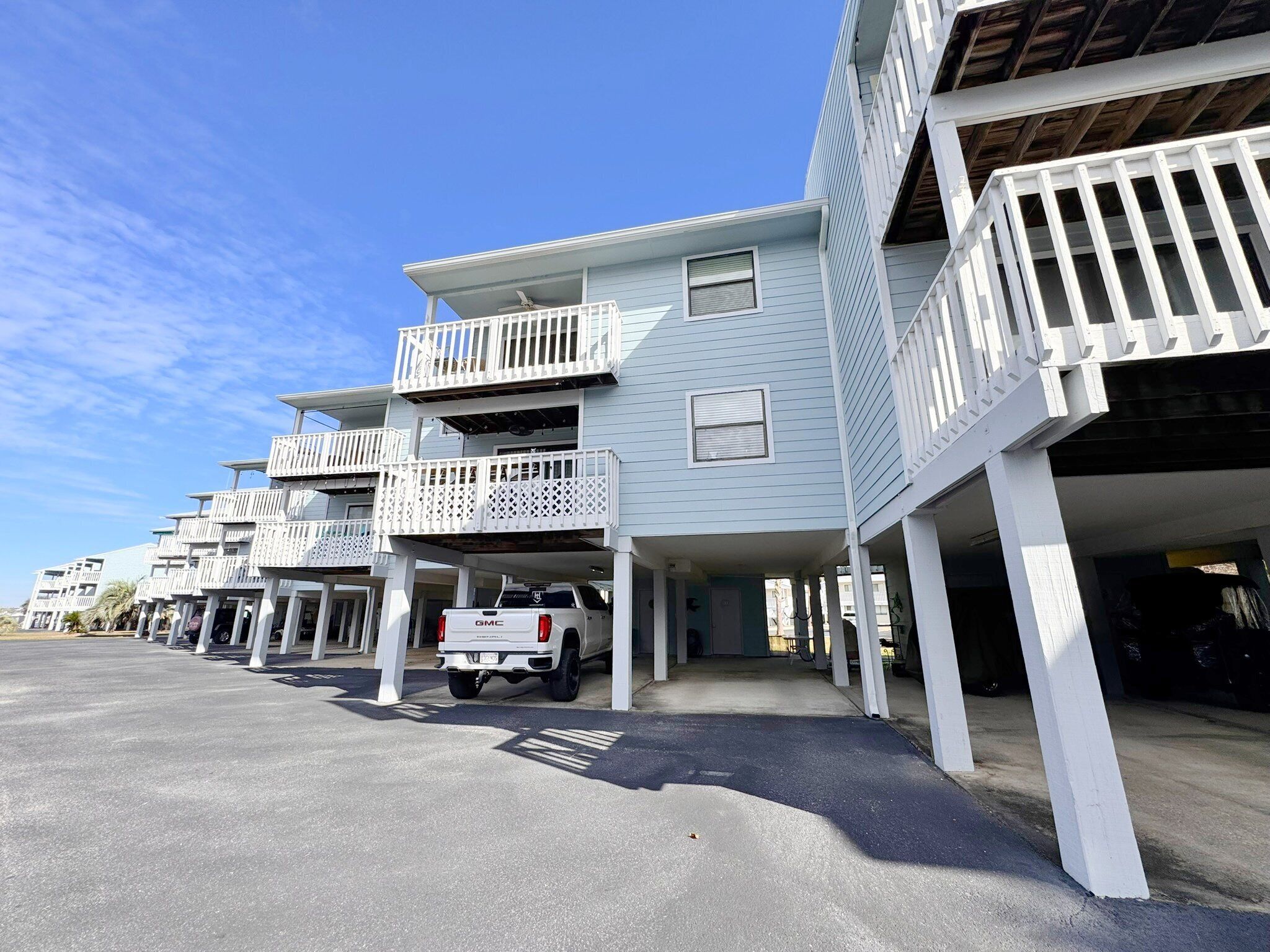 A row of light blue multi-story buildings with white balconies and a white pickup truck parked in front.