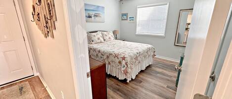 A bedroom with a bed, a ceiling fan, a window with blinds, and a door.