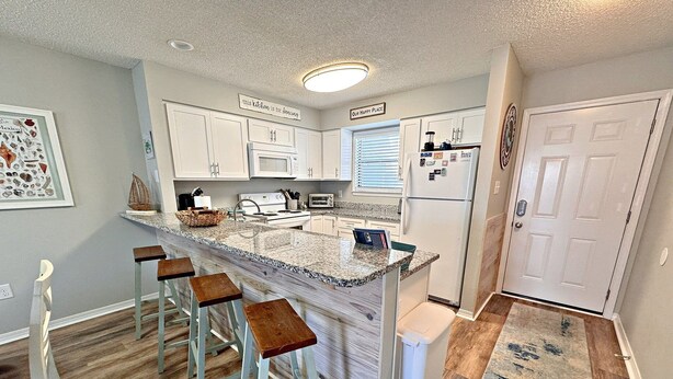 A kitchen with a central island, bar stools, a refrigerator, and a microwave. - Come get your toes in the sand! Enjoy the Vitamin Sea ☀️ (Orange Beach)
