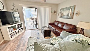 A living room with a brown leather sofa, a television, a bookshelf, and a ceiling fan. - Come get your toes in the sand! Enjoy the Vitamin Sea ☀️ (Orange Beach)