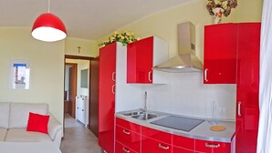 Uma cozinha compacta com armários vermelhos, bancada branca e luminária pendente vermelha.