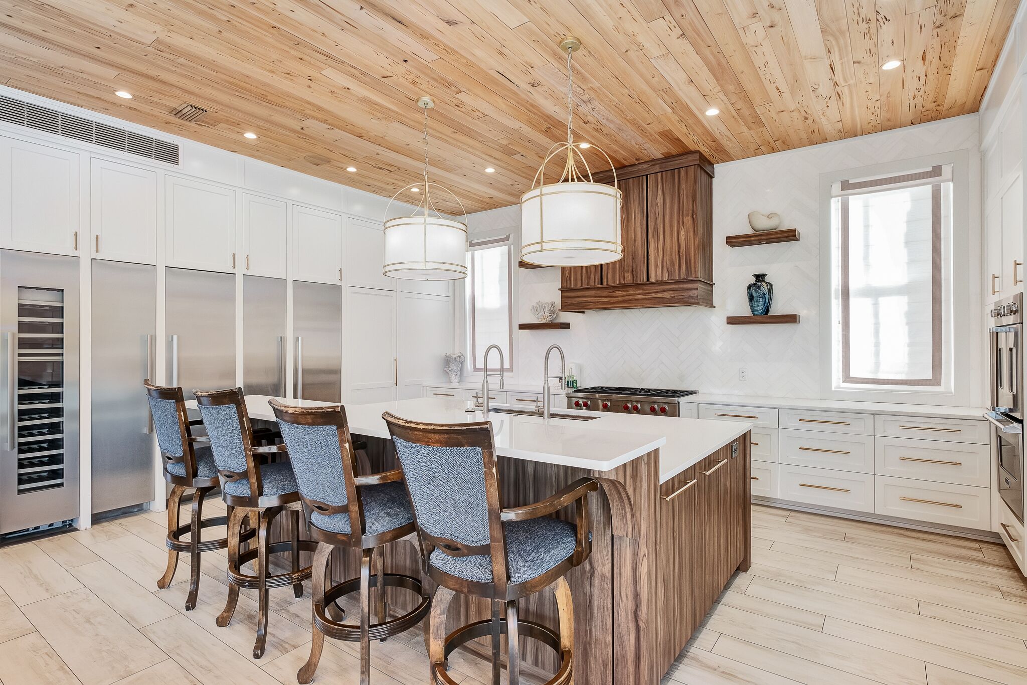 Een moderne keuken met houten plafond, witte kasten, een centraal eiland met barstoelen en geïntegreerde apparatuur.