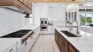 A modern kitchen with white cabinetry, a stainless steel range, and a large island with a sink. - Paradise at Park Row|Easy Beach Access|Large Resort Style Private Pool (Destin)