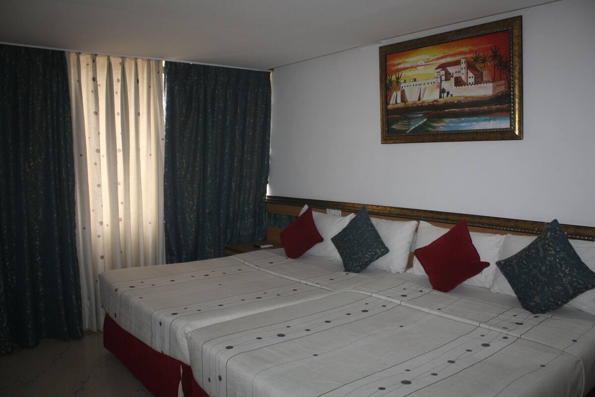 Una habitació d'hotel amb un llit gran, un quadre a la paret i cortines a la finestra.