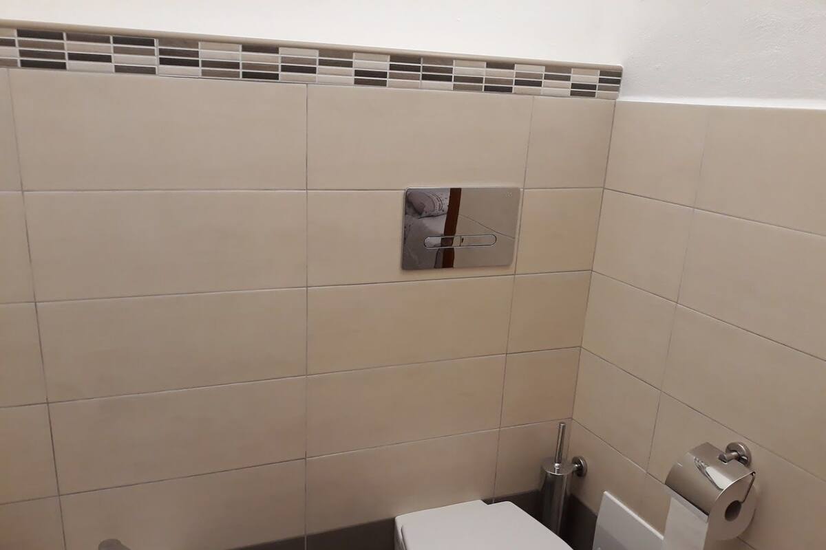 Une petite salle de bain moderne avec des toilettes blanches, un lavabo doté d’un robinet chromé et un porte-rouleau de papier toilette.