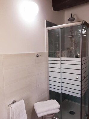 A modern bathroom with a glass-enclosed shower, a white tiled wall, and a small stool with a towel. - Al Pez Exclusive Rooms (Olbia)