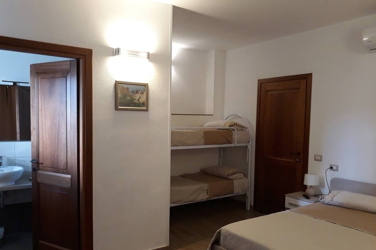 Une chambre avec un lit superposé, une table de chevet avec une lampe et une porte donnant sur une salle de bain.