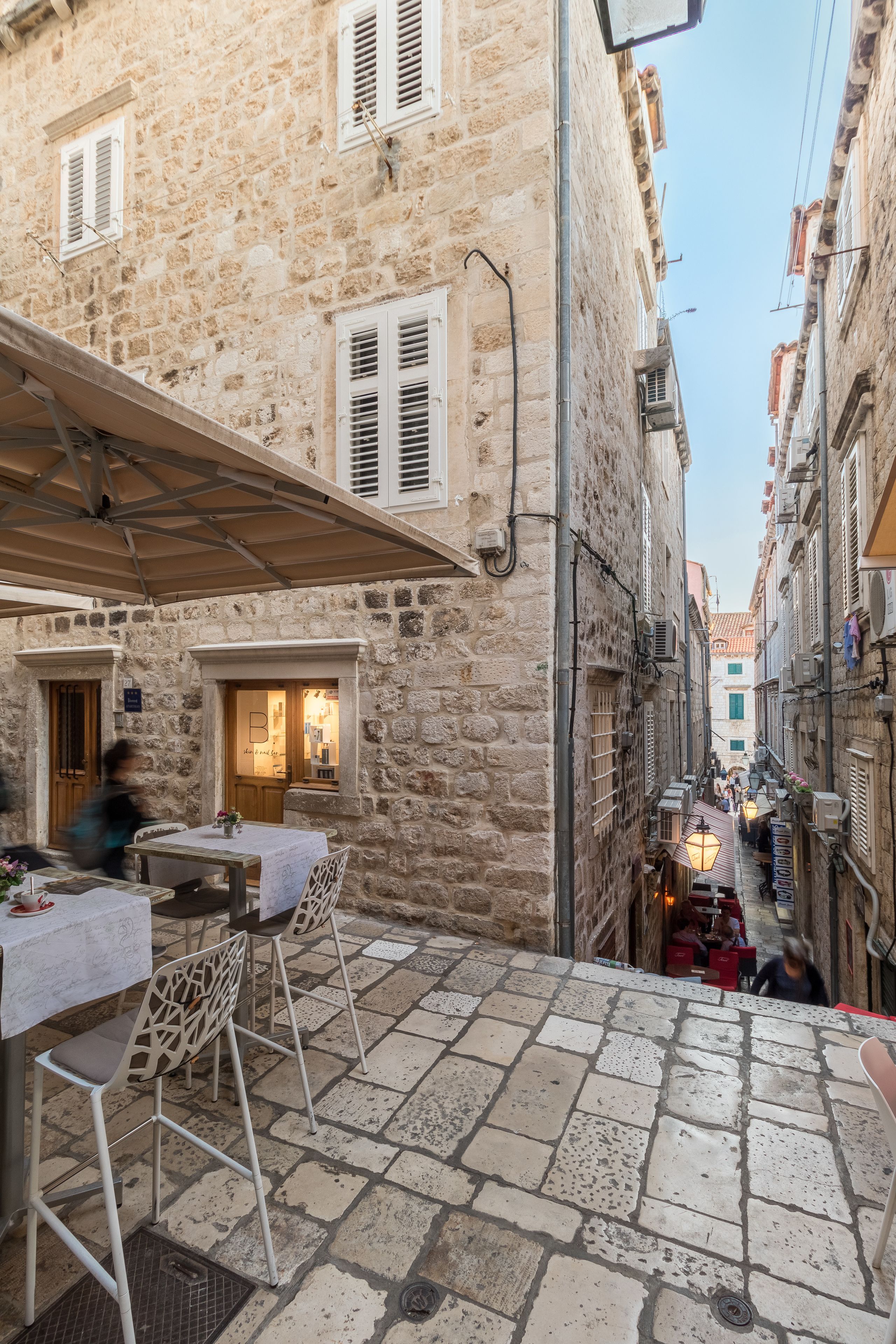 A narrow stone street with outdoor seating, a café, and a building with a visible entrance.
