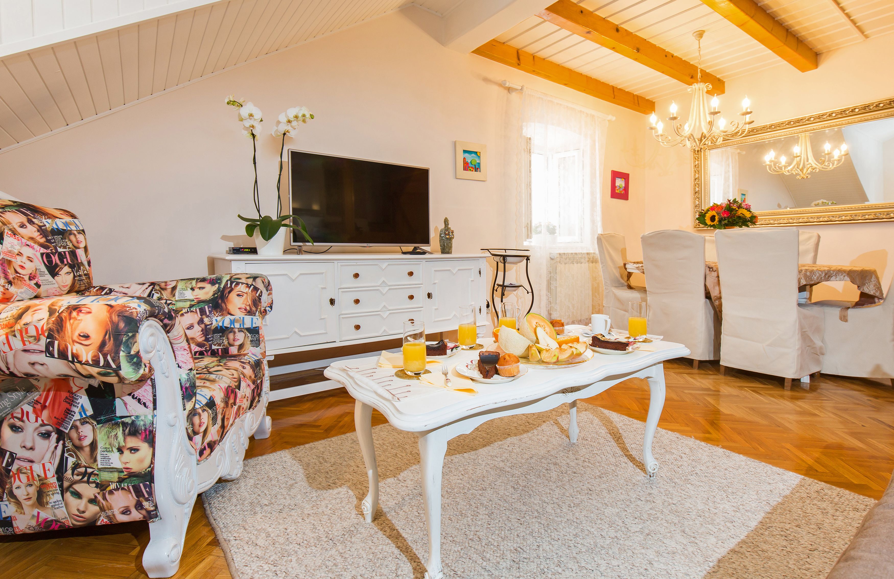 A living room with a white sofa, a coffee table with breakfast items, a TV, and a chandelier.