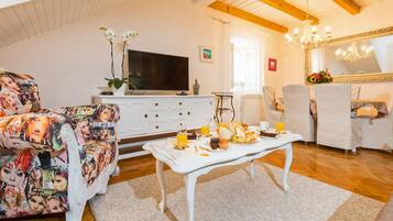 A living room with a white sofa, a coffee table with breakfast items, a TV, and a chandelier.