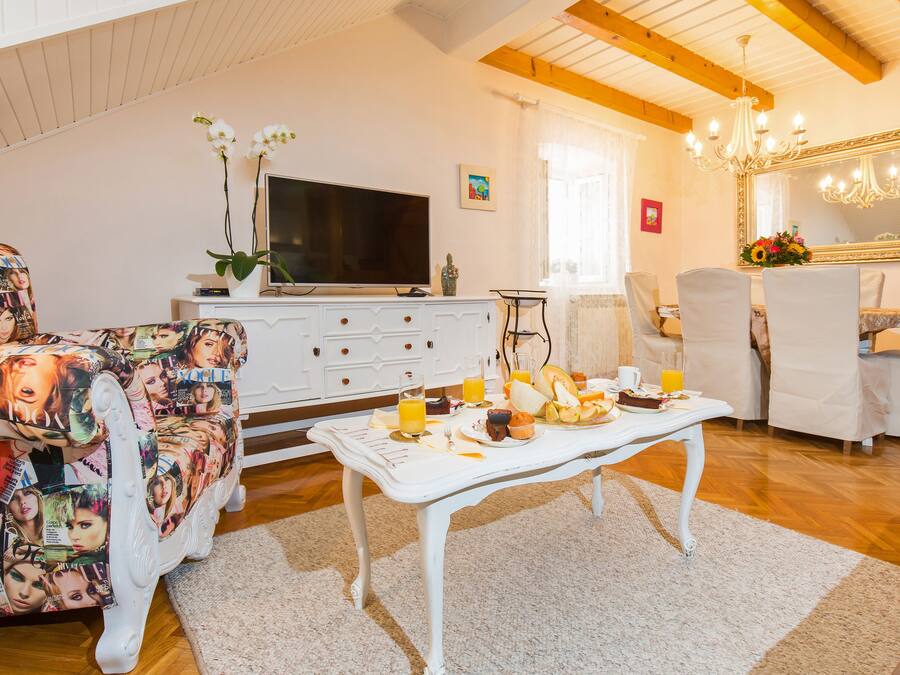 A living room with a white sofa, a coffee table with breakfast items, a TV, and a chandelier.