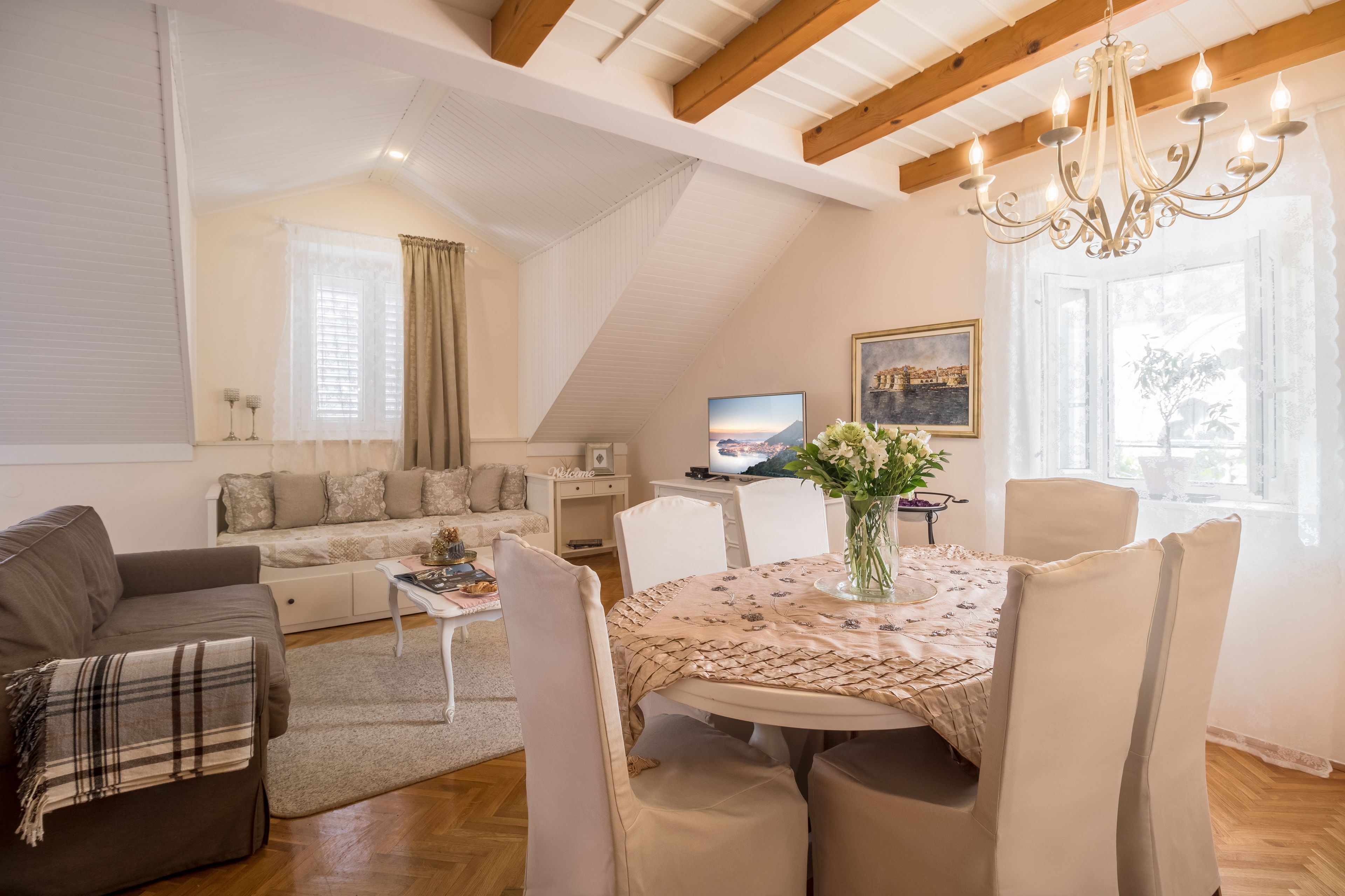 Een ruime woonkamer met een hoge plafond, een eethoek met een tafel gedekt voor vier personen, en een gezellige zithoek met een bank en fauteuils.
