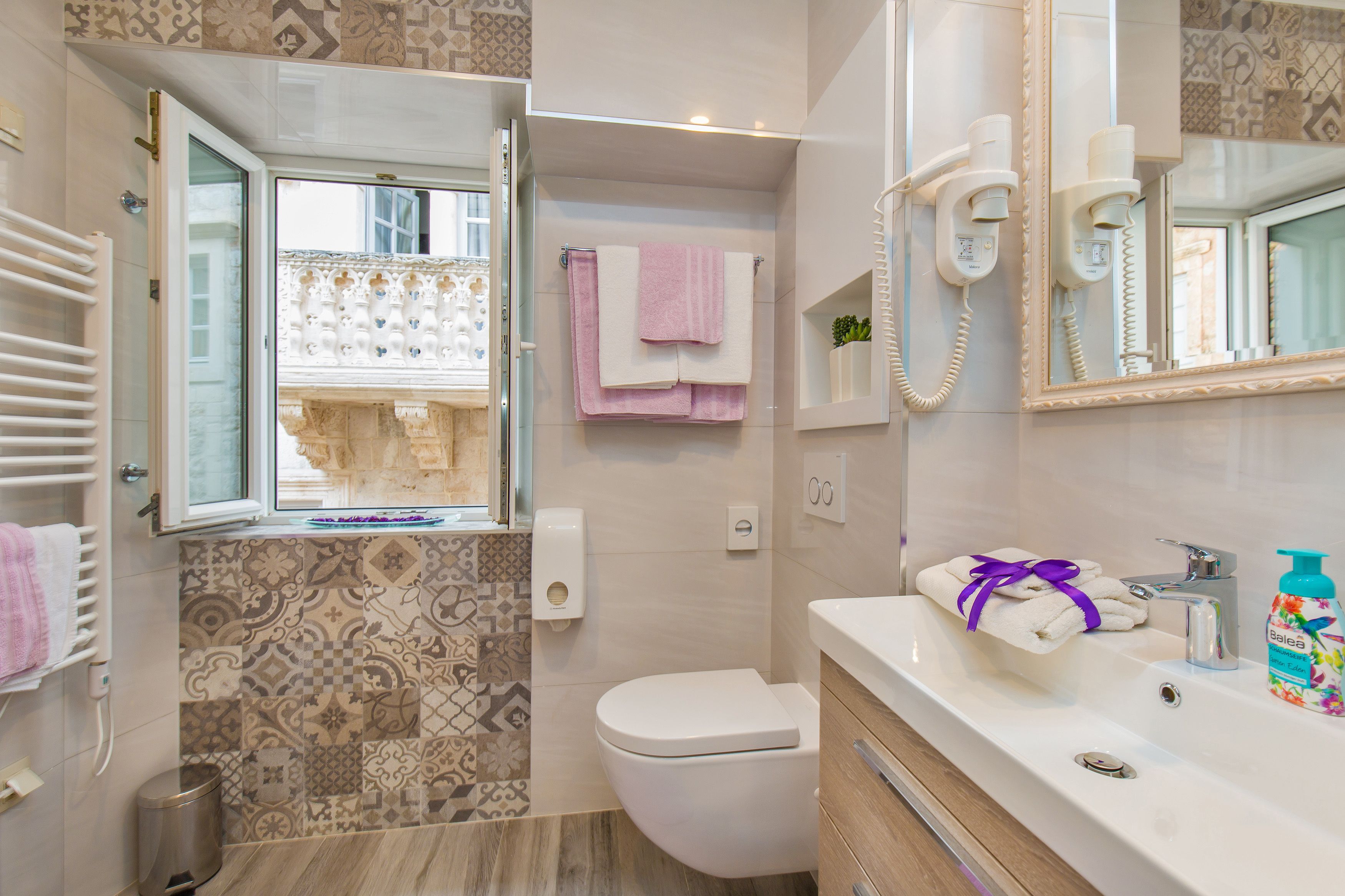 A bathroom with a toilet, sink, and a window with patterned tiles.