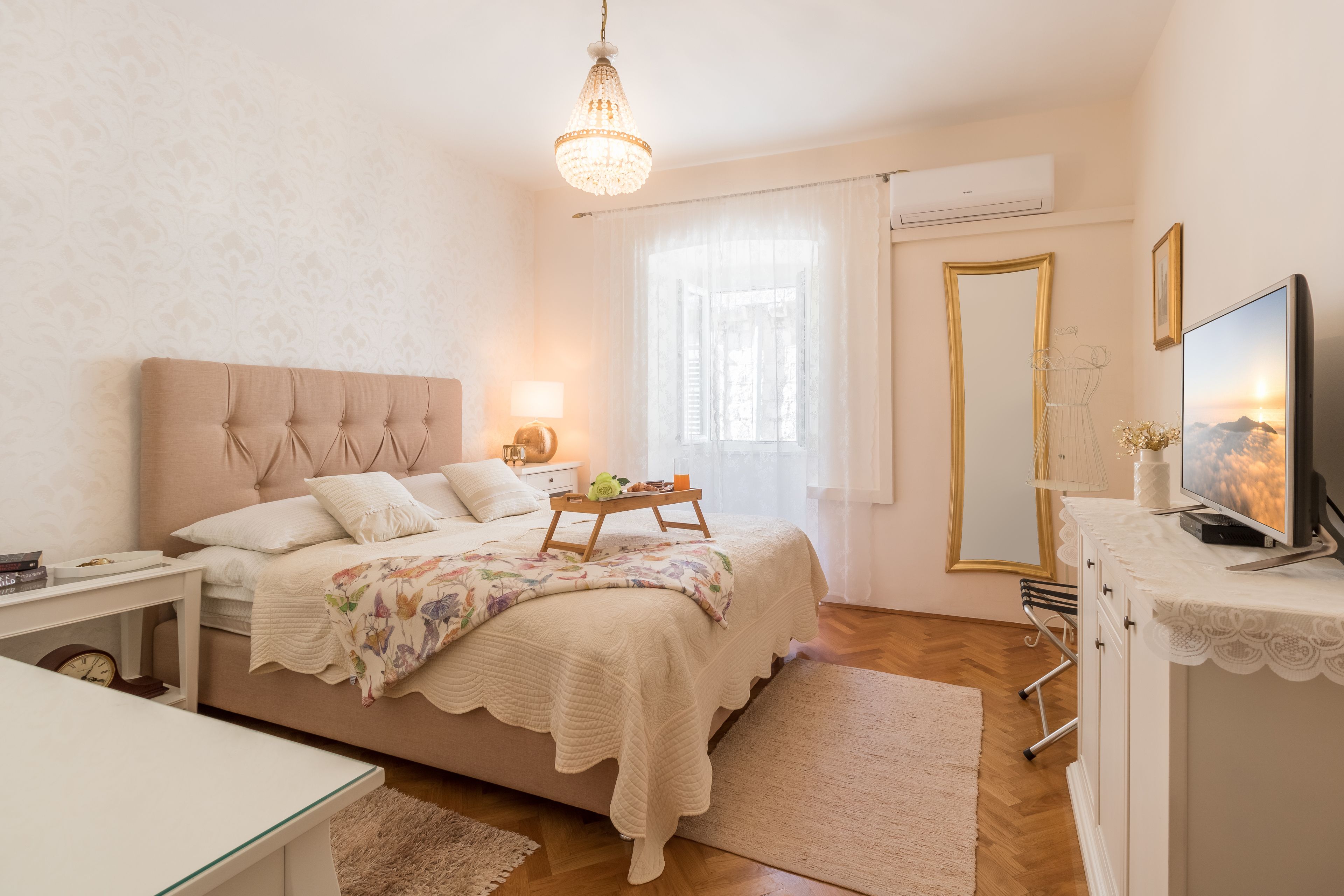 Une chambre à coucher avec un lit, une table de chevet, une lampe, une télévision et une fenêtre avec des rideaux.