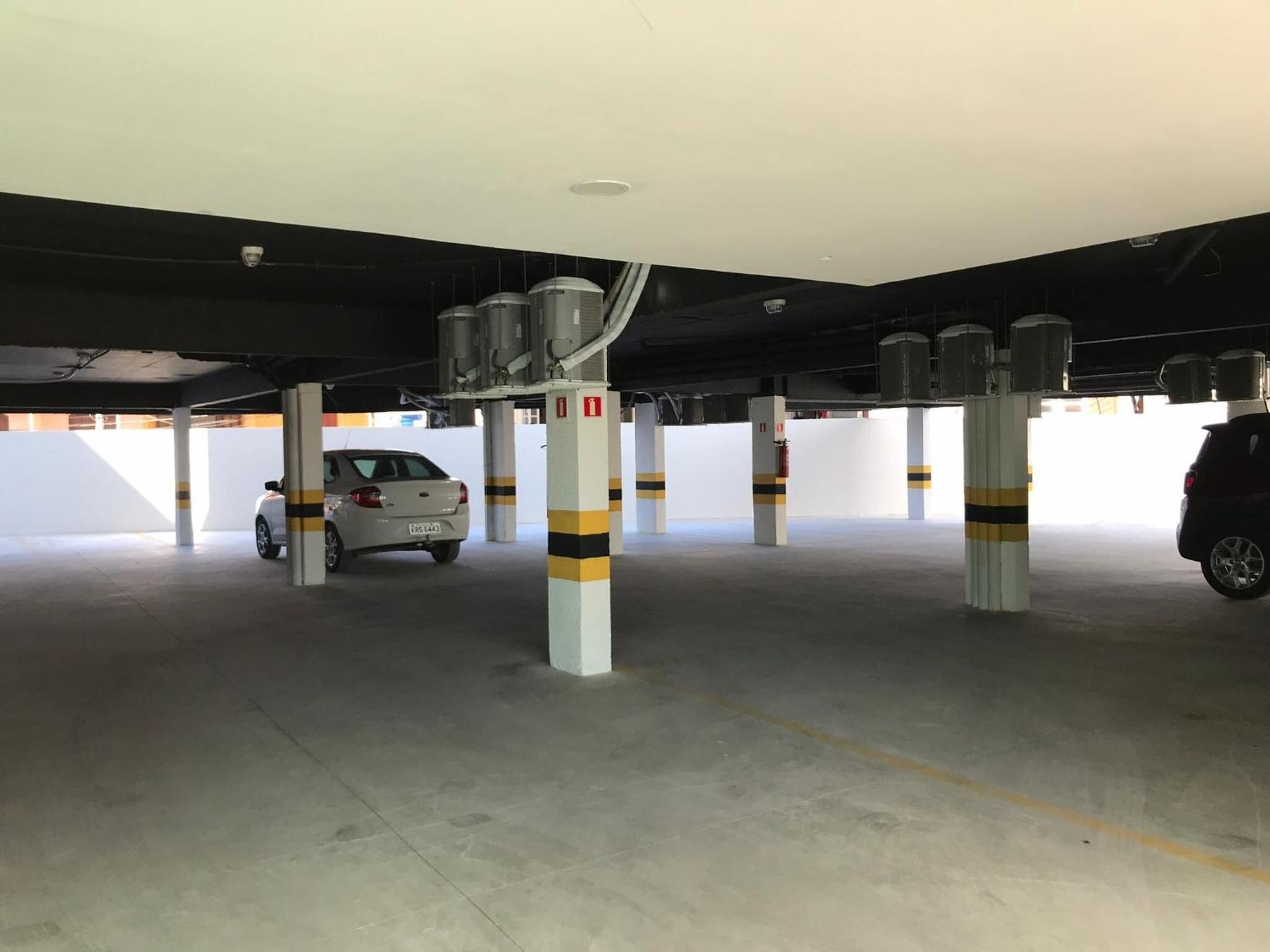 A parking garage with concrete pillars, a white car, and a black car parked.