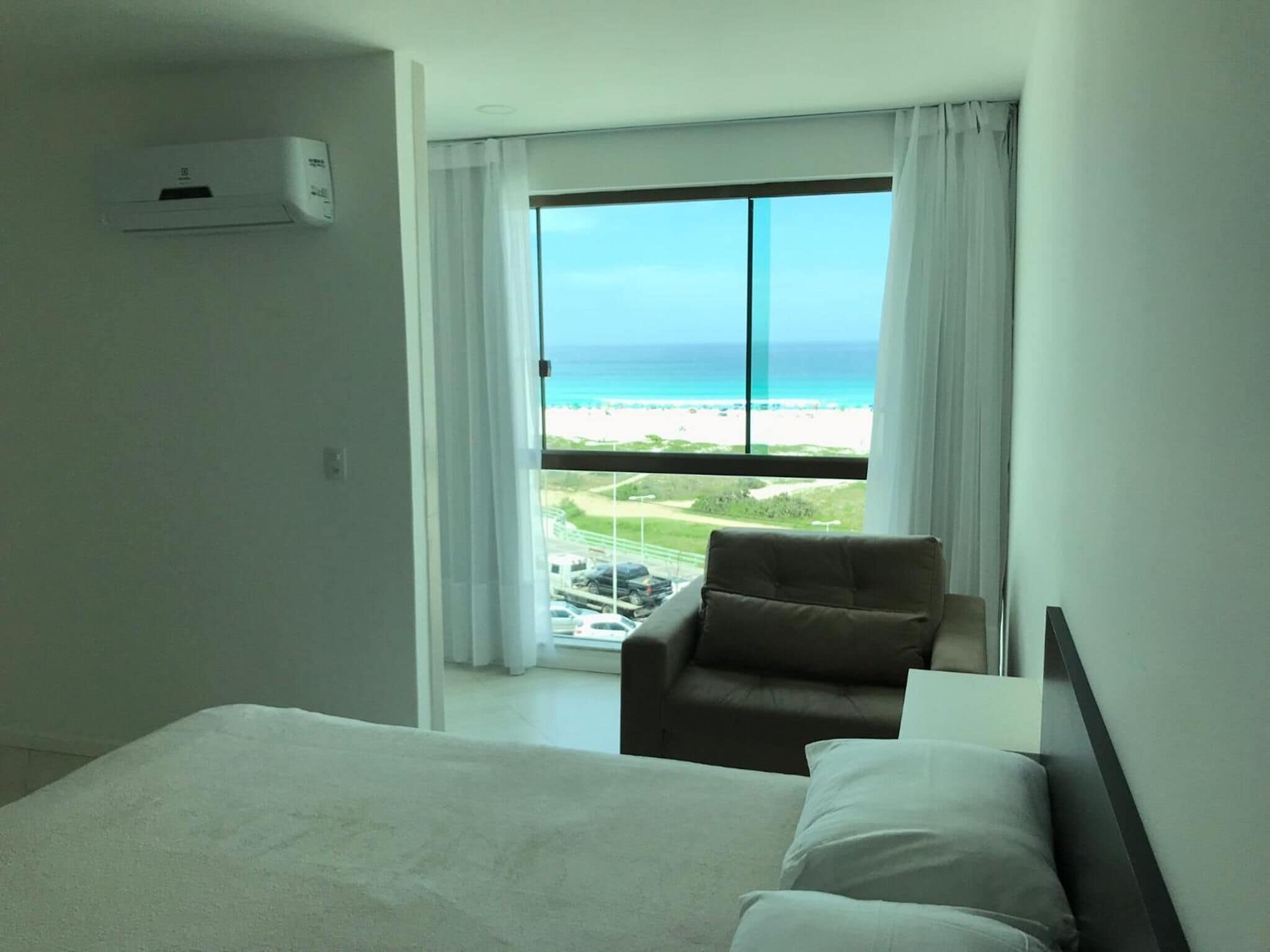 A hotel room with a bed, a chair, and a large window offering a view of the beach and ocean.