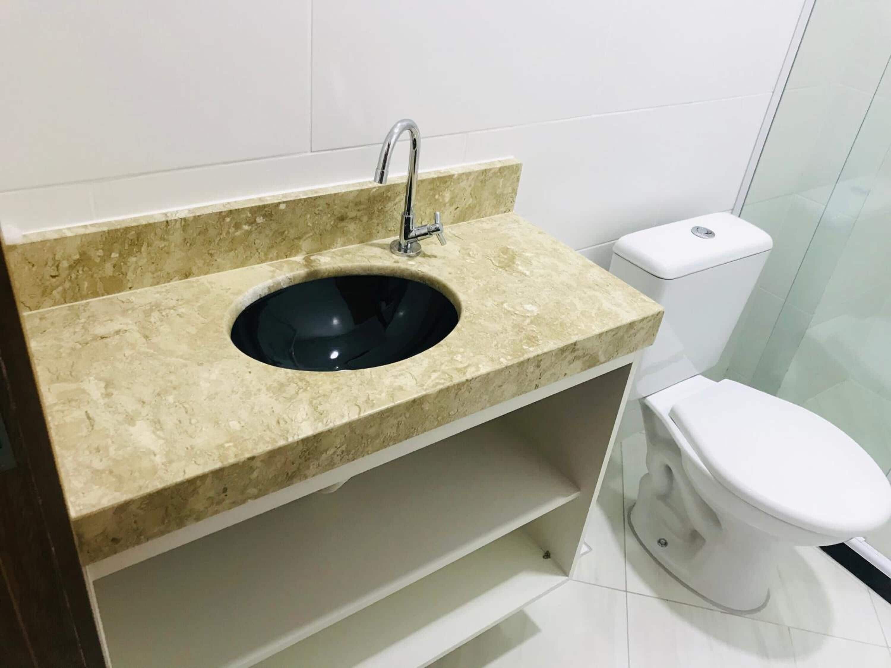 A bathroom with a beige marble sink, a modern faucet, and a white toilet.