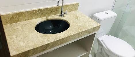A bathroom with a beige marble sink, a modern faucet, and a white toilet.
