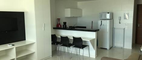 A modern living room with a flat-screen TV, a sofa, and a dining area with chairs.