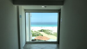 A hallway with a large glass door leading to a balcony with a view of the beach. - Sophia II Residence Inn (Arraial do Cabo)