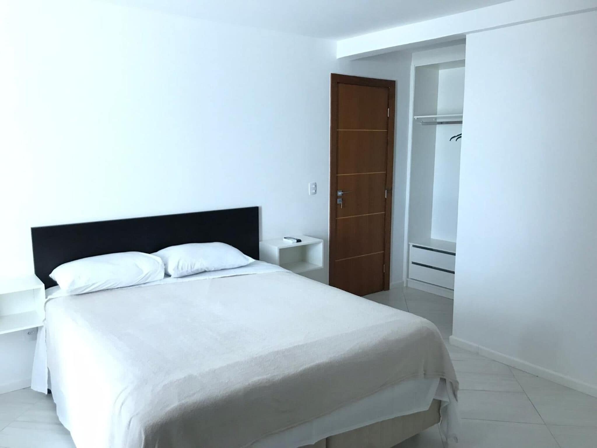 Quarto com cama, mesa de cabeceira, porta de madeira e closet espaçoso.